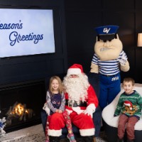 Little girl sits on Santa's lap and little brother smiles big on the chair in front of Louie